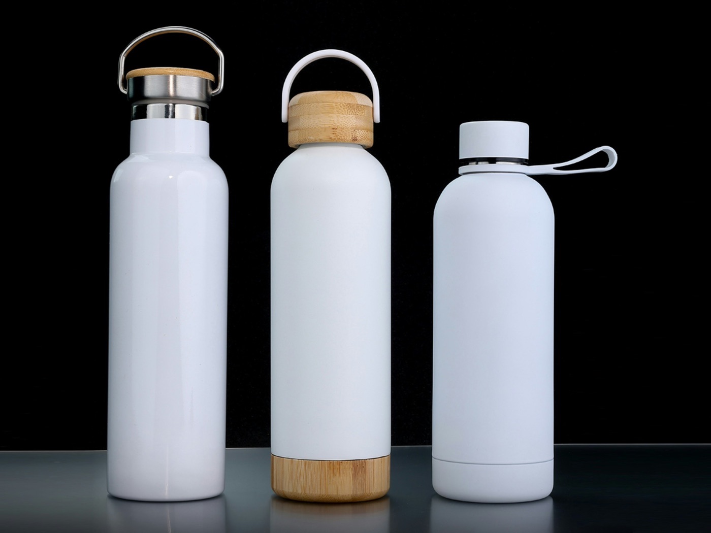 Three blank white insulated bottles with bamboo lids, lined up ready for decoration
