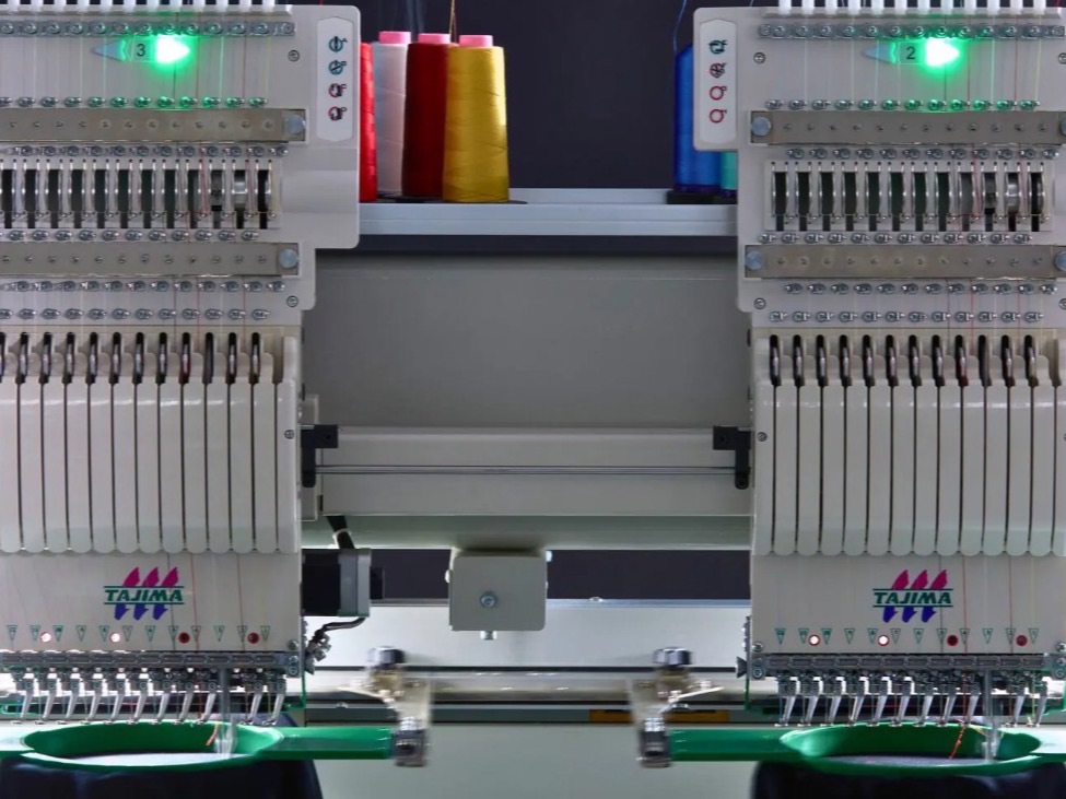 Two Tajima embroidery heads threaded and running, with cones of coloured thread racked behind them