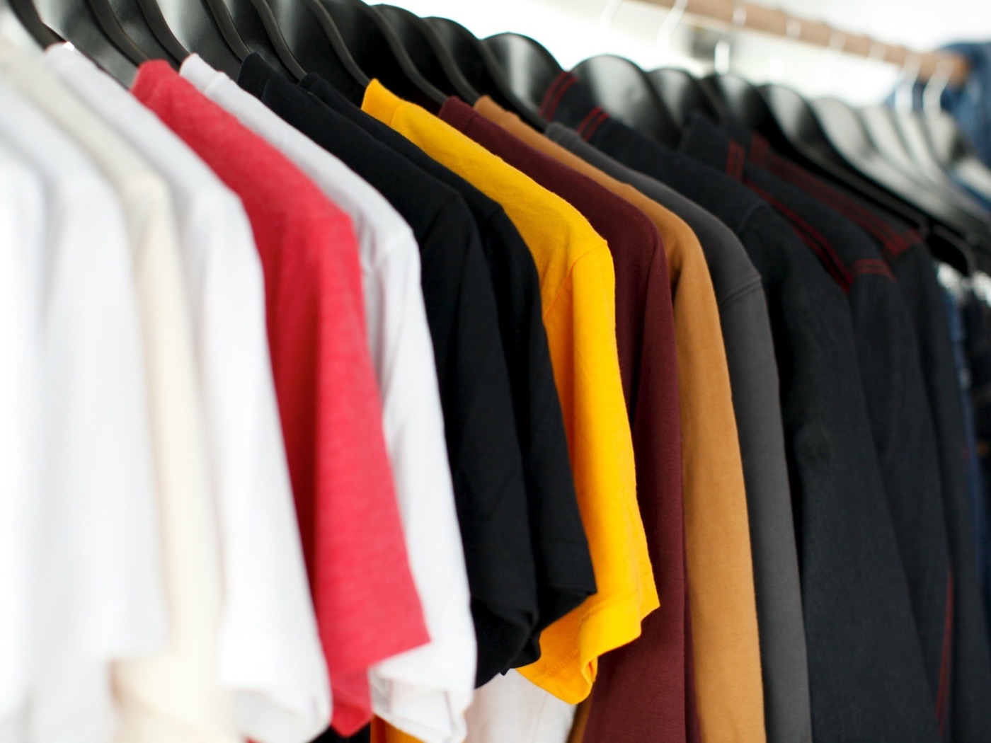 Rack of shirts in white, red, black, gold, maroon, and tan hanging ready for print